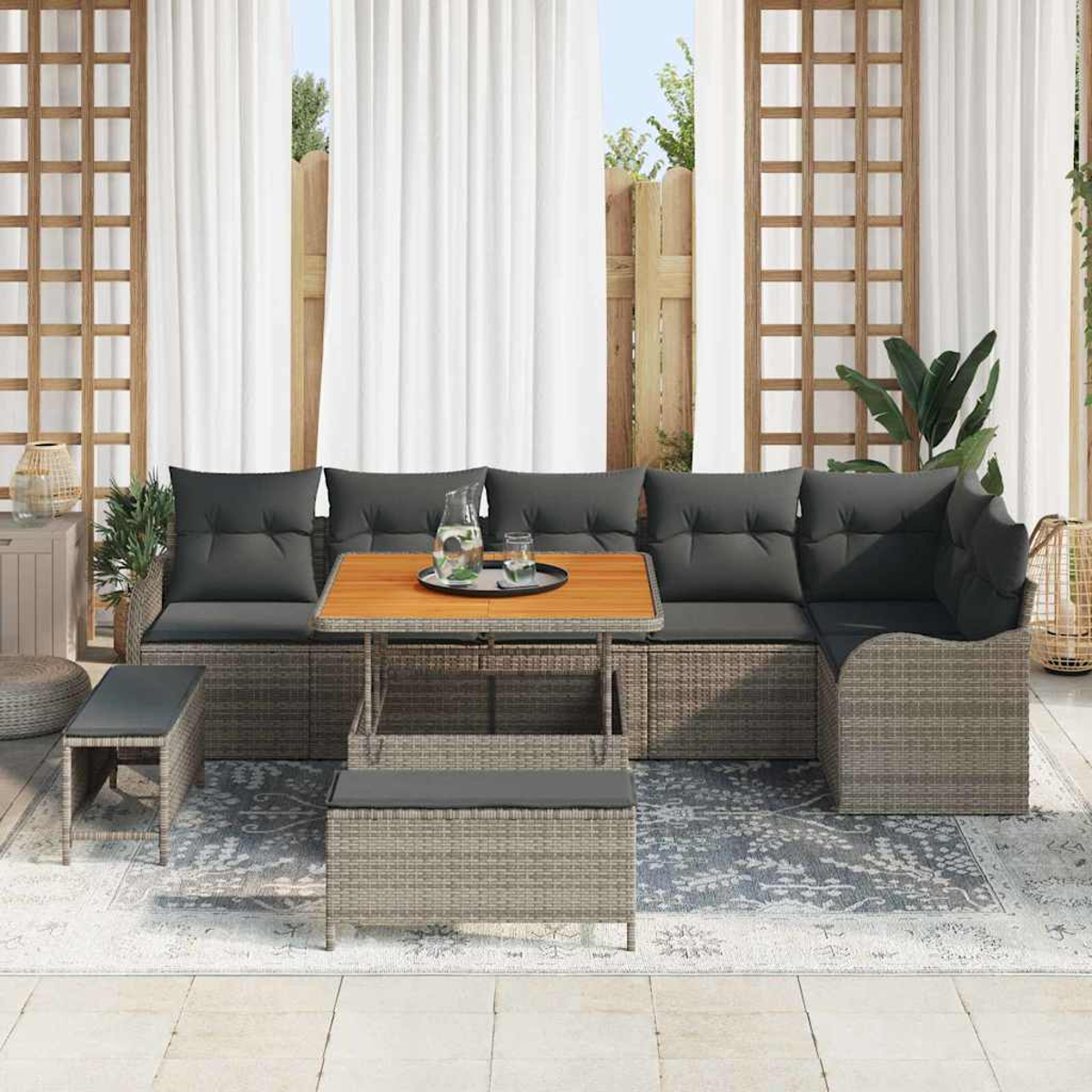 Gartenmöbel-Set mit grauen Kissen und einem Holztisch. Hintergrund: weiße Vorhänge und Holzzaun.