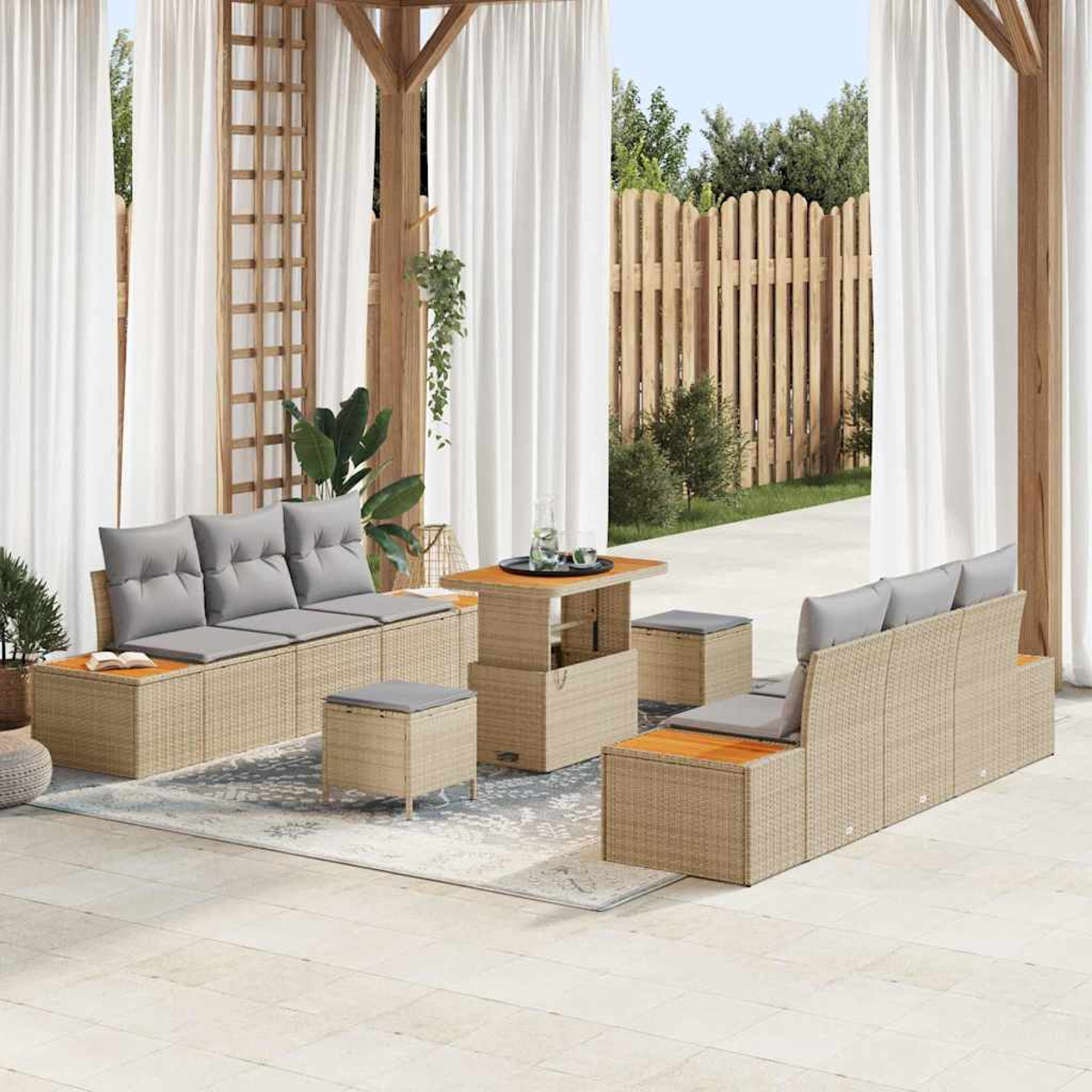 Terrassengarnitur mit Korbs Sofas, grauen Kissen, Holztisch und Hockern. Weiße Vorhänge und Holzzaun im Hintergrund.