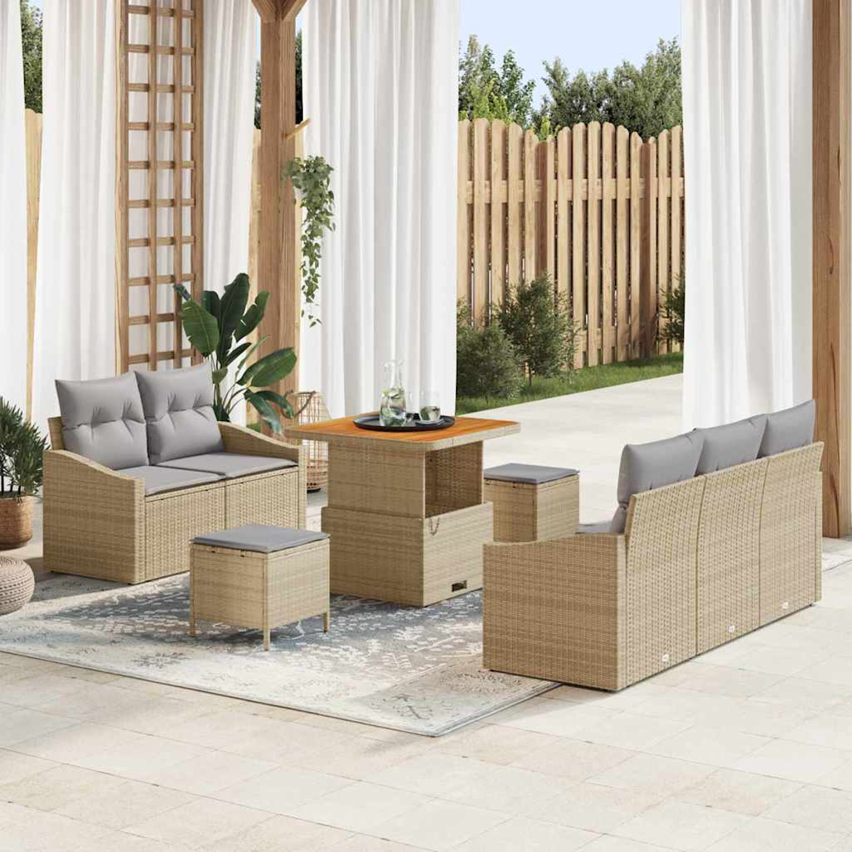 Terrassenset: Korbmöbel, Sofa, Liebesitz, Hocker und Tisch mit grauen Kissen. Weiße Vorhänge und Holzzaun im Hintergrund.