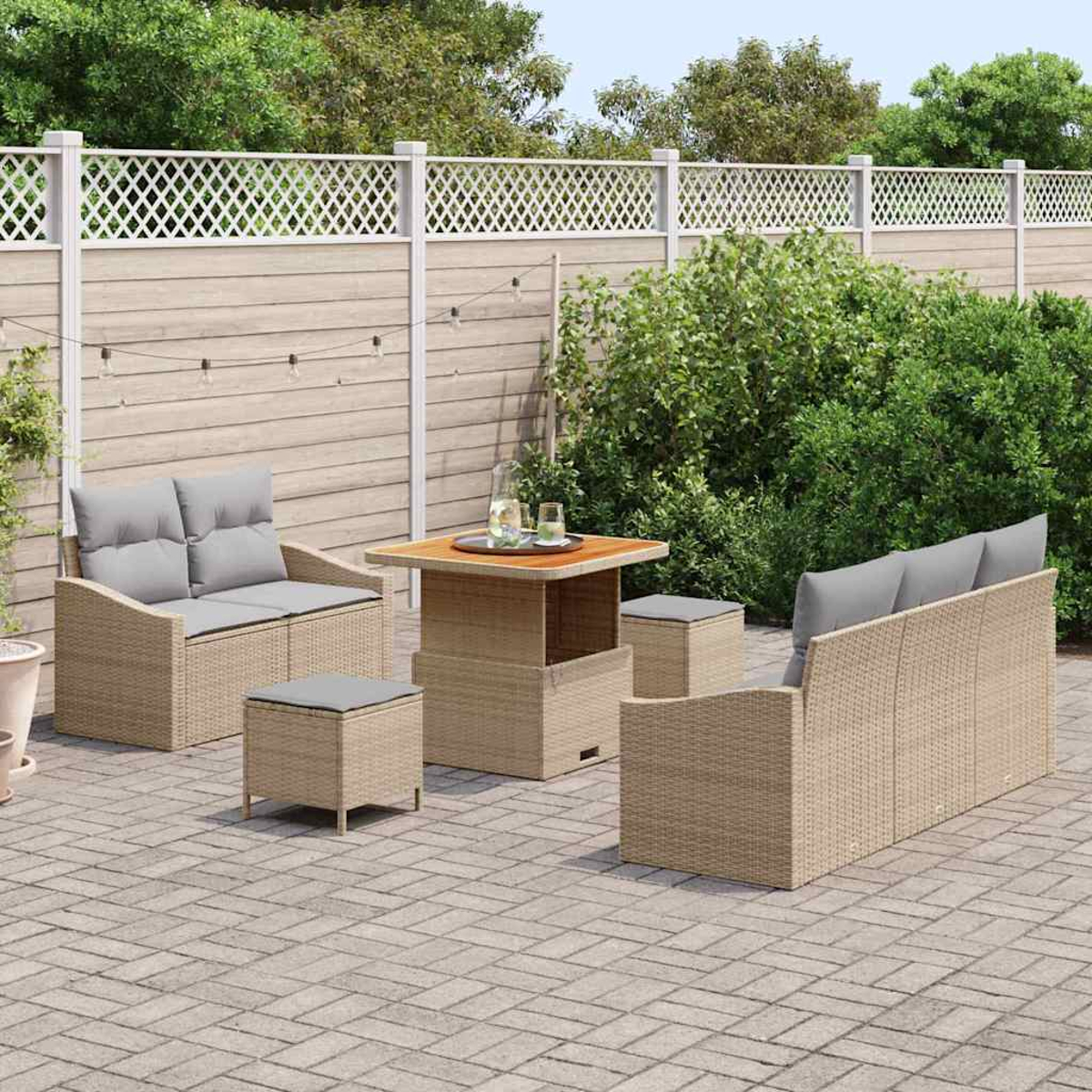 Garten-Terrassenset mit Tisch, Sofa, zwei Stühlen und zwei Ottomanen. Das Set steht auf einer gepflasterten Terrasse, im Hintergrund ein Holzzaun.