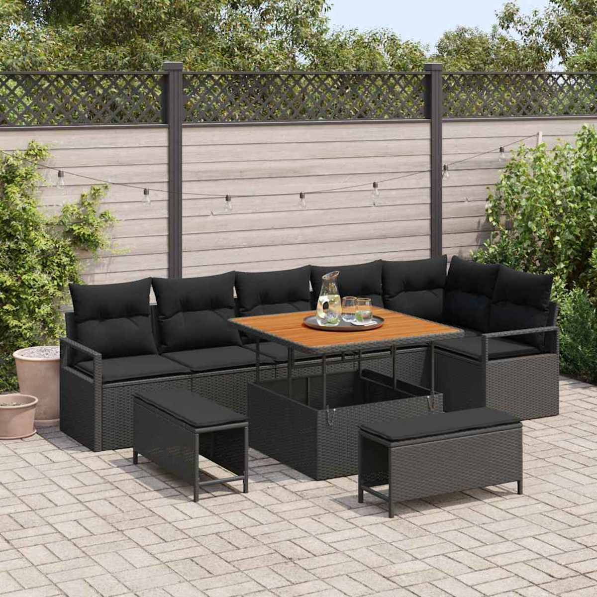 Garten-Sitzgruppe mit schwarzen Kissen und einem Holztisch. Enthält Bänke. Im Hintergrund sind ein Zaun und Pflanzen zu sehen.