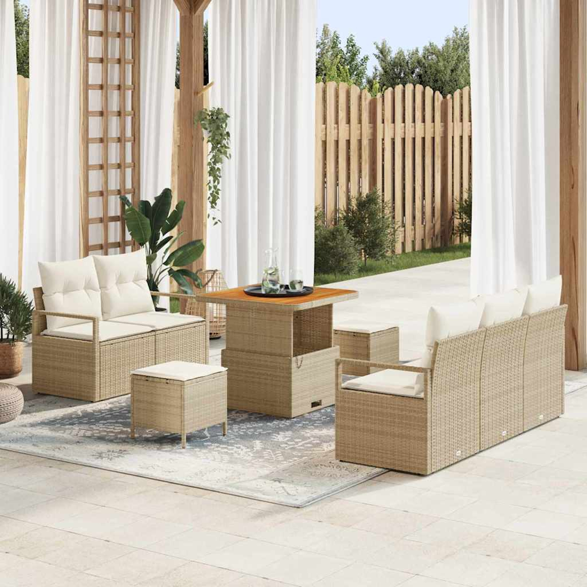 Terrassenset mit beigen Korbmöbeln, weißen Kissen und einem Holztisch. Weiße Vorhänge und ein Holzzaun im Hintergrund.