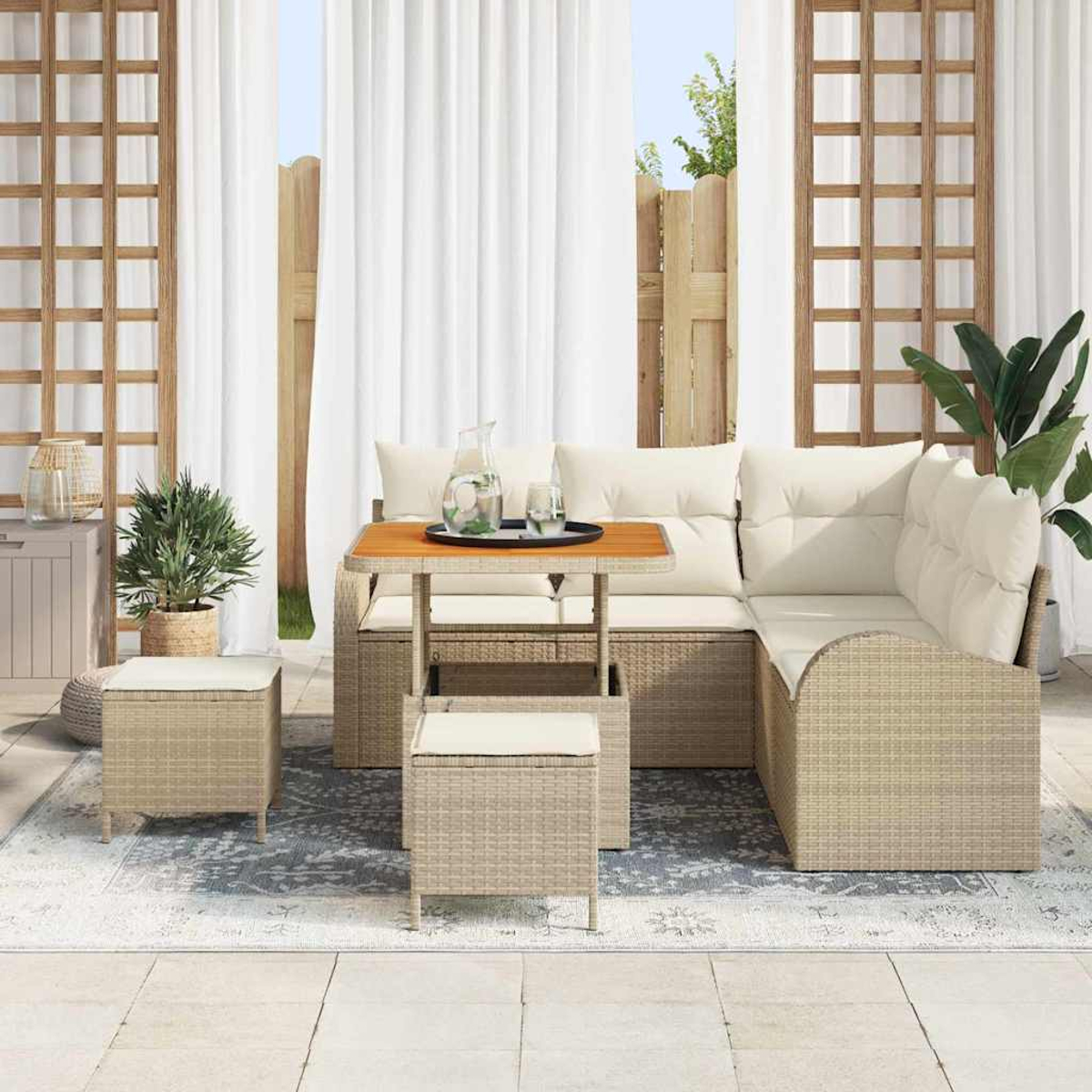 Terrassengarnitur mit Sofa, zwei Hockern, Tisch und Pflanzen. Weiße Vorhänge und Holzzaun im Hintergrund.