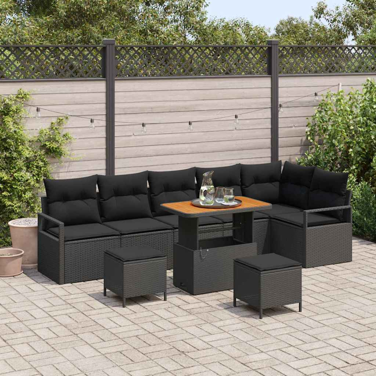 Garten-Sitzgruppe mit schwarzen Kissen und einem Holztisch. Auf dem Tisch stehen eine Kanne und Gläser. Die Umgebung ist eine Terrasse.