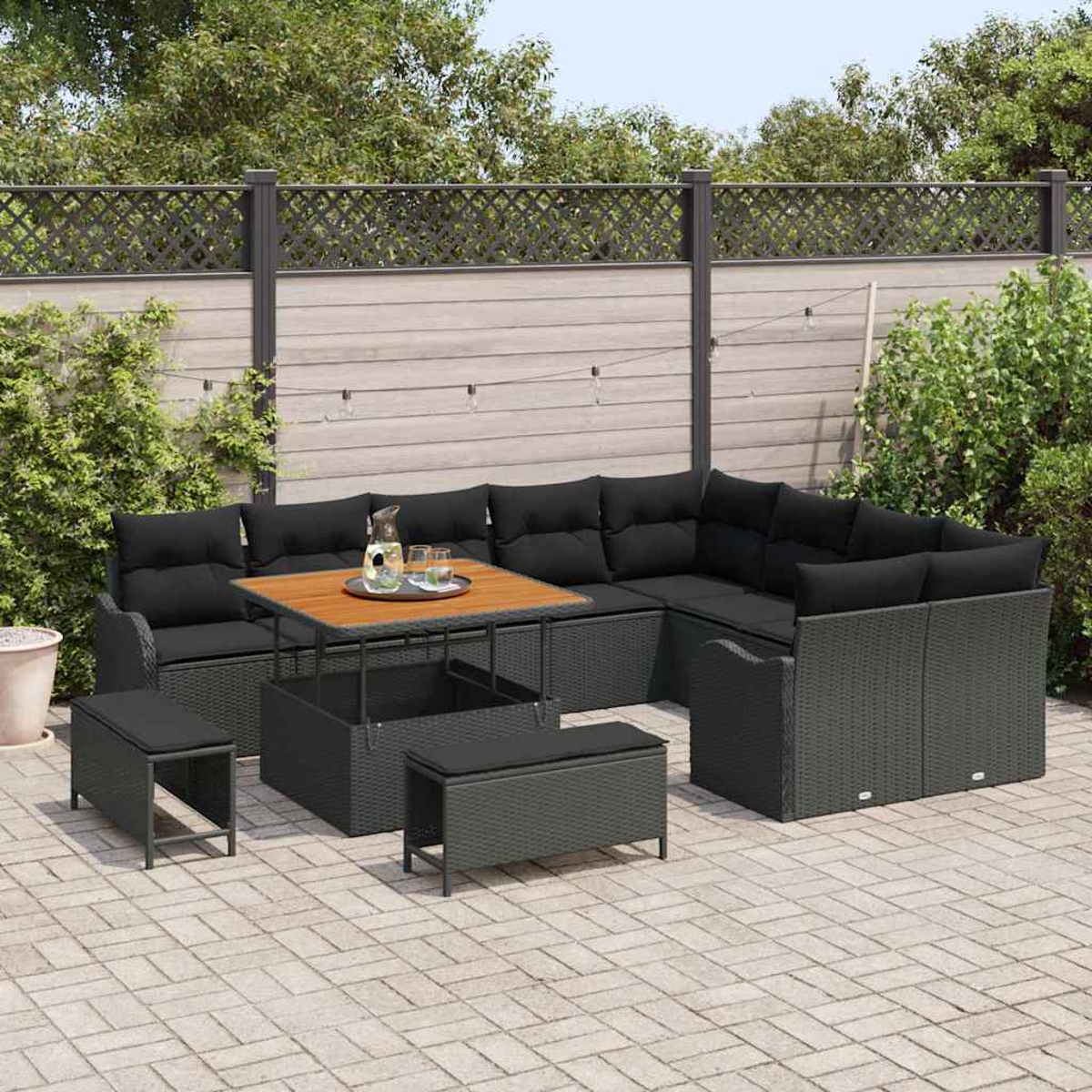Garten-Sitzgruppe mit schwarzen Kissen, einem Holztisch und zwei Bänken auf einer Backstein-Terrasse. Im Hintergrund ein Holzzaun.