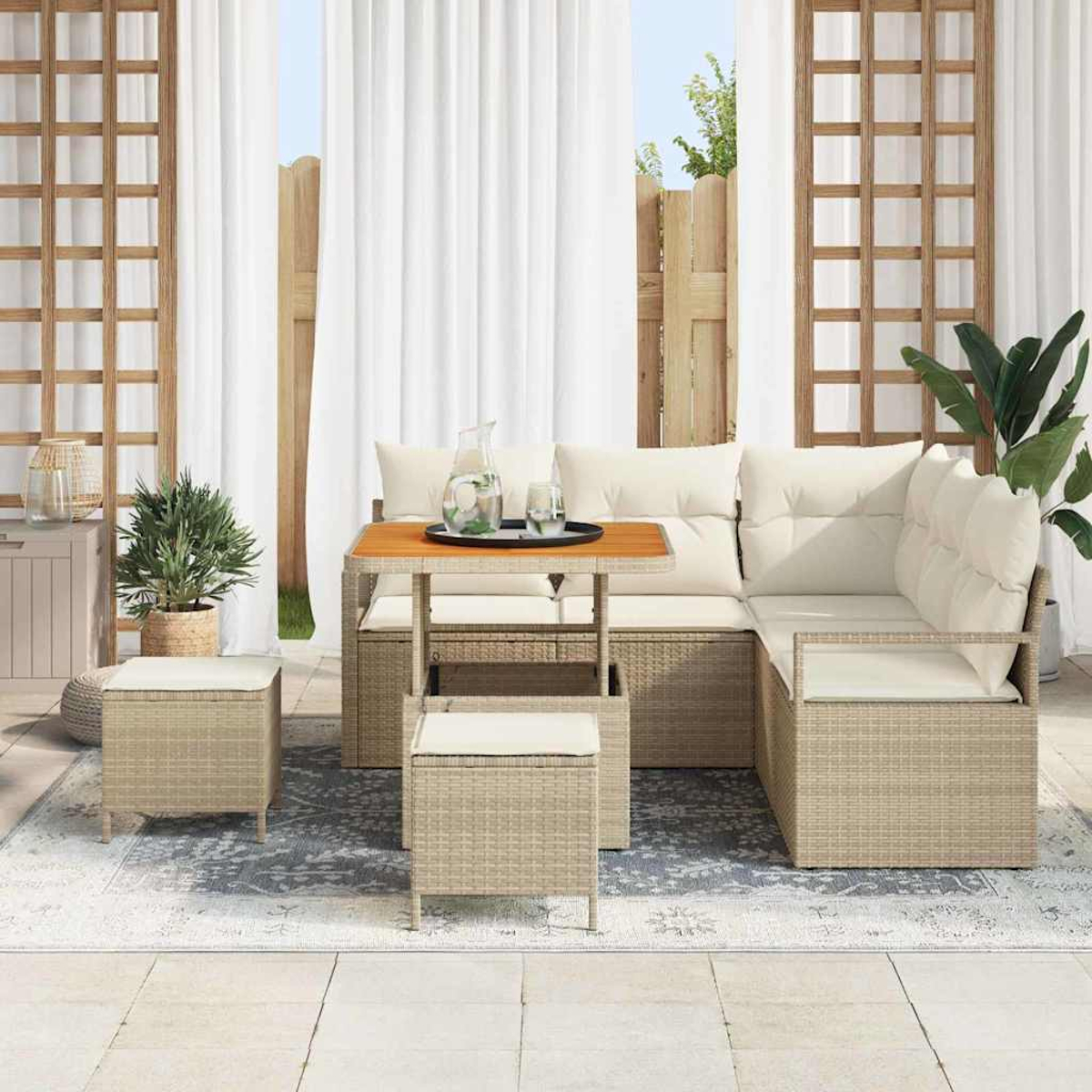 Outdoor-Sitzbereich mit beigen Korbmöbeln, weißen Kissen, Holztisch und weißen Vorhängen im Hintergrund.