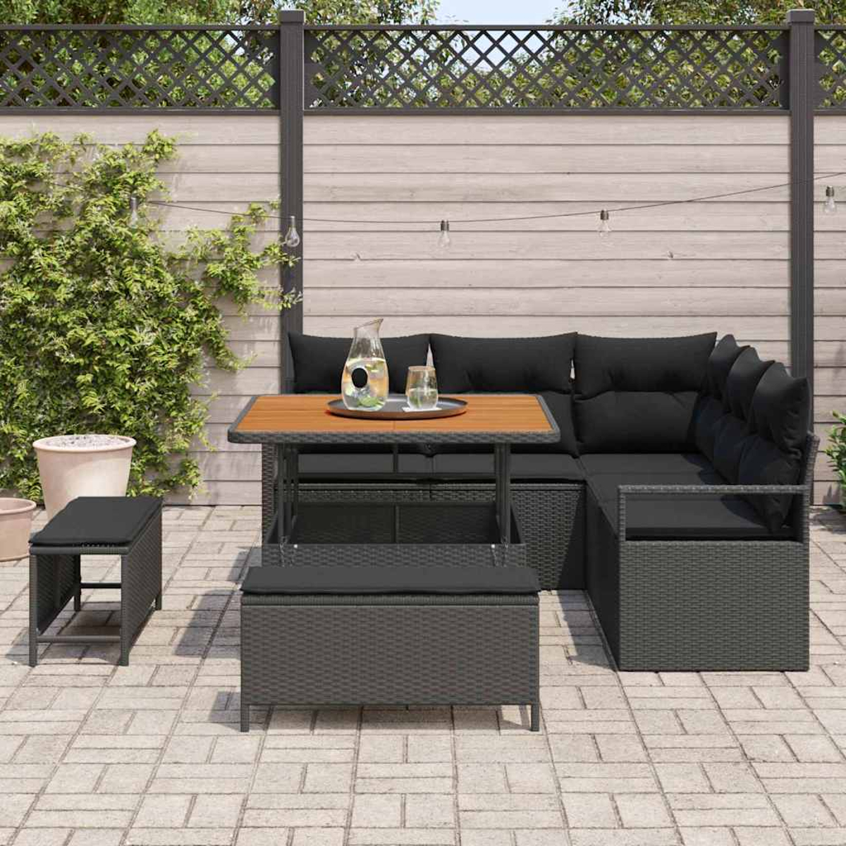Garten-Sitzgruppe mit Tisch, Stühlen und einer Bank. Schwarze Kissen und Korbmöbel. Inklusive Wasserkrug und Gläser auf dem Tisch.