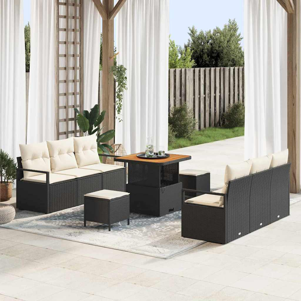 Terrassenset mit schwarzem Korbmöbel, beigen Kissen, quadratischem Tisch und weißen Vorhängen. Hintergrund mit Zaun und Grün.
