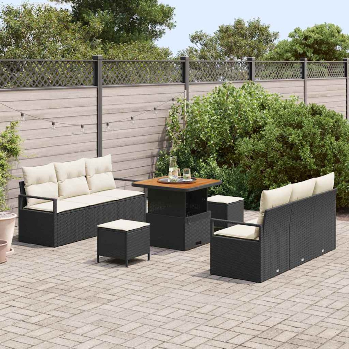 Terrassengarnitur: schwarze Korbmöbel mit cremefarbenen Kissen. Enthält einen Tisch, zwei Sofas und zwei Ottomanen auf einer gepflasterten Terrasse.