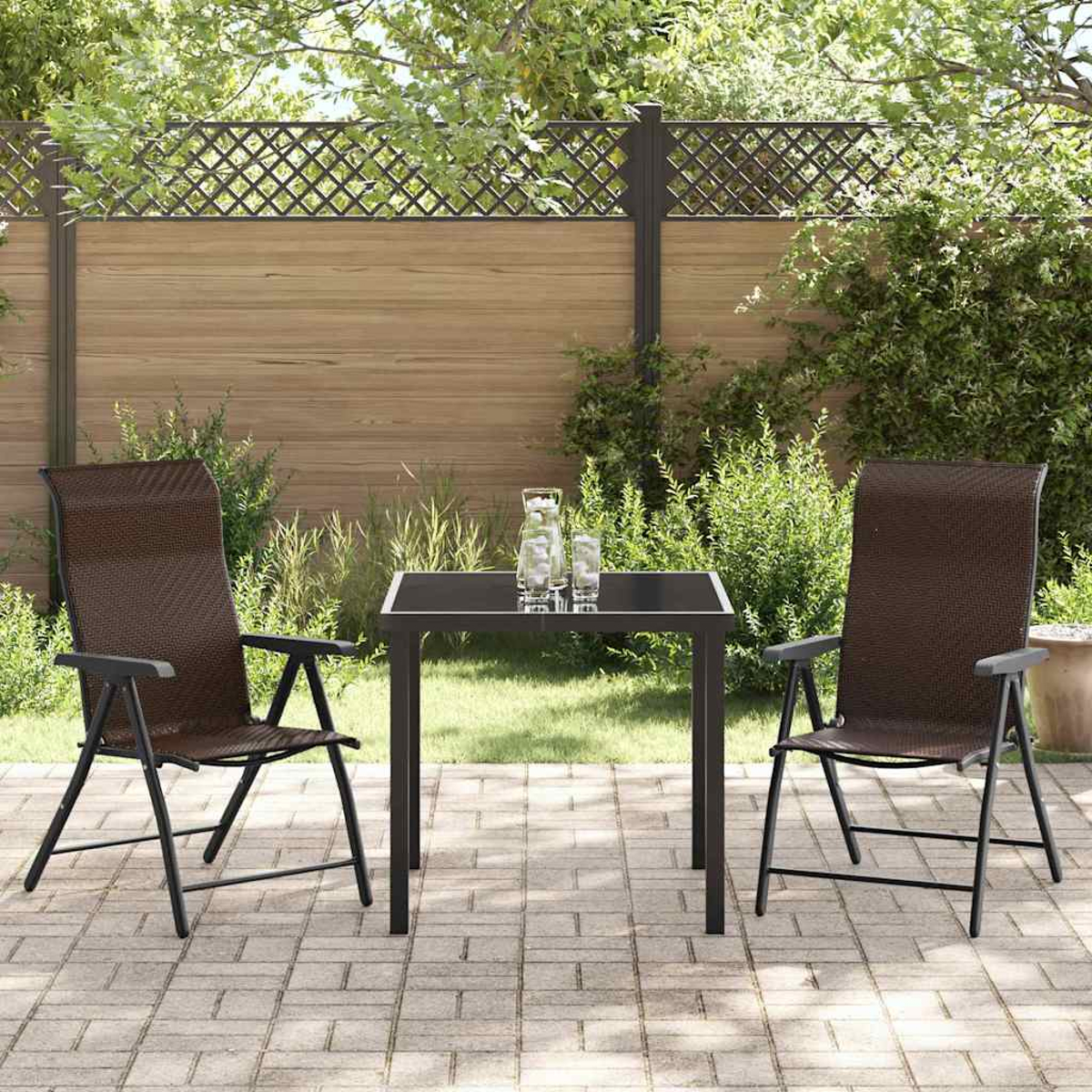 Terrassenszene mit zwei braunen Stühlen, einem Tisch und zwei Gläsern. Grüne Büsche, ein Holzzaun und ein Gitter im Hintergrund.