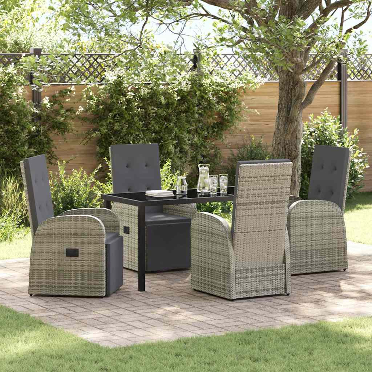 Set da patio esterno: tavolo quadrato, quattro sedie, bicchieri e brocca su un patio in mattoni, con alberi e recinzione sullo sfondo.