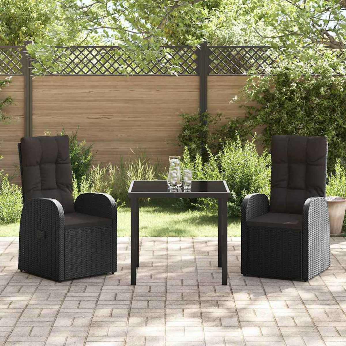 Schwarze Korbstühle mit Kissen und ein kleiner Tisch auf einer Terrasse. Im Hintergrund ein Holzzaun und Grün.