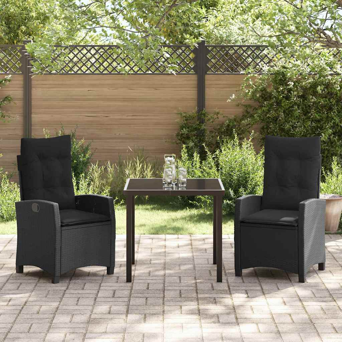 Set da patio esterno con due sedie nere e un tavolo. Sullo sfondo una recinzione e delle piante.