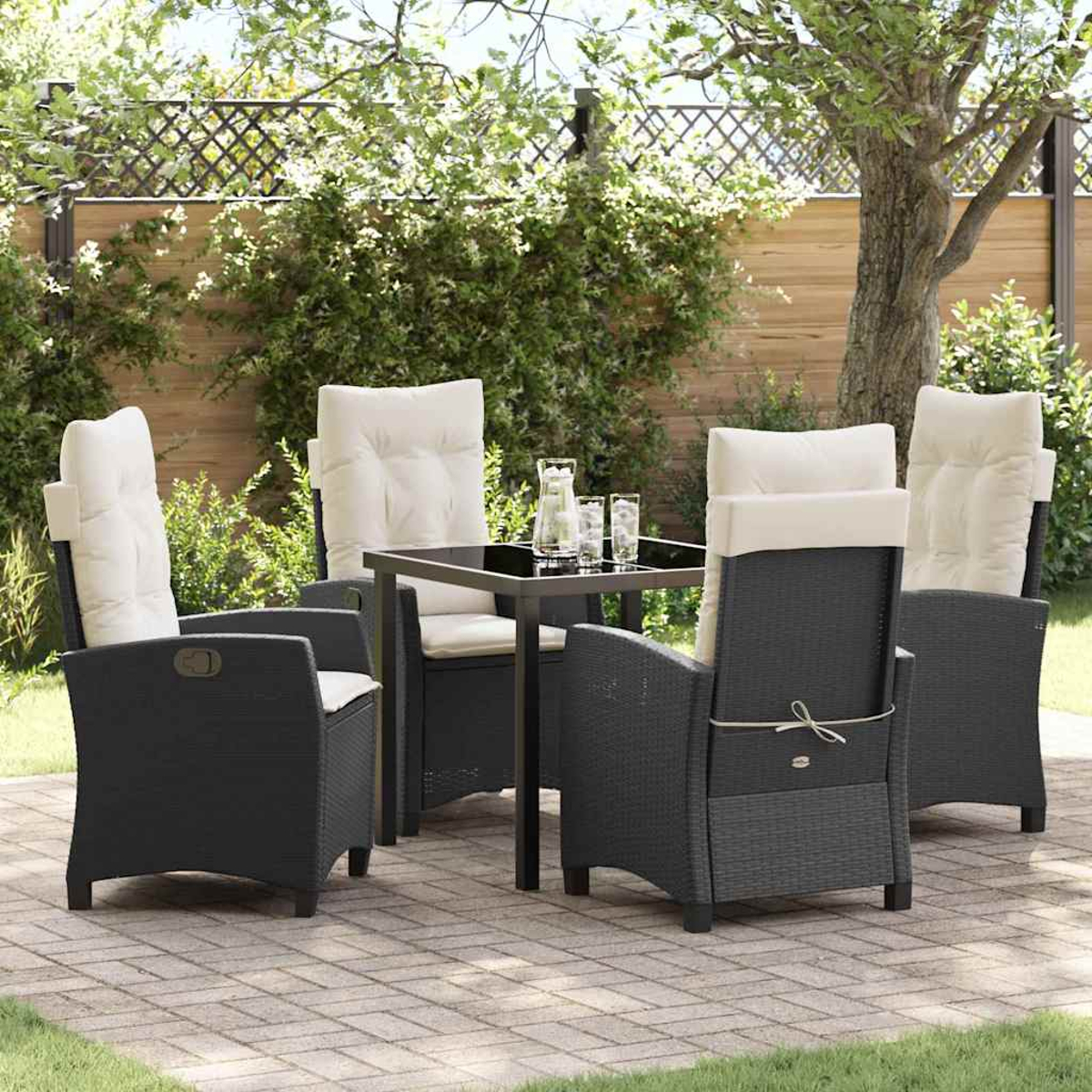 Garten-Set mit vier schwarzen Korbstühlen mit cremefarbenen Kissen um einen quadratischen Tisch. Grünes Laub im Hintergrund.