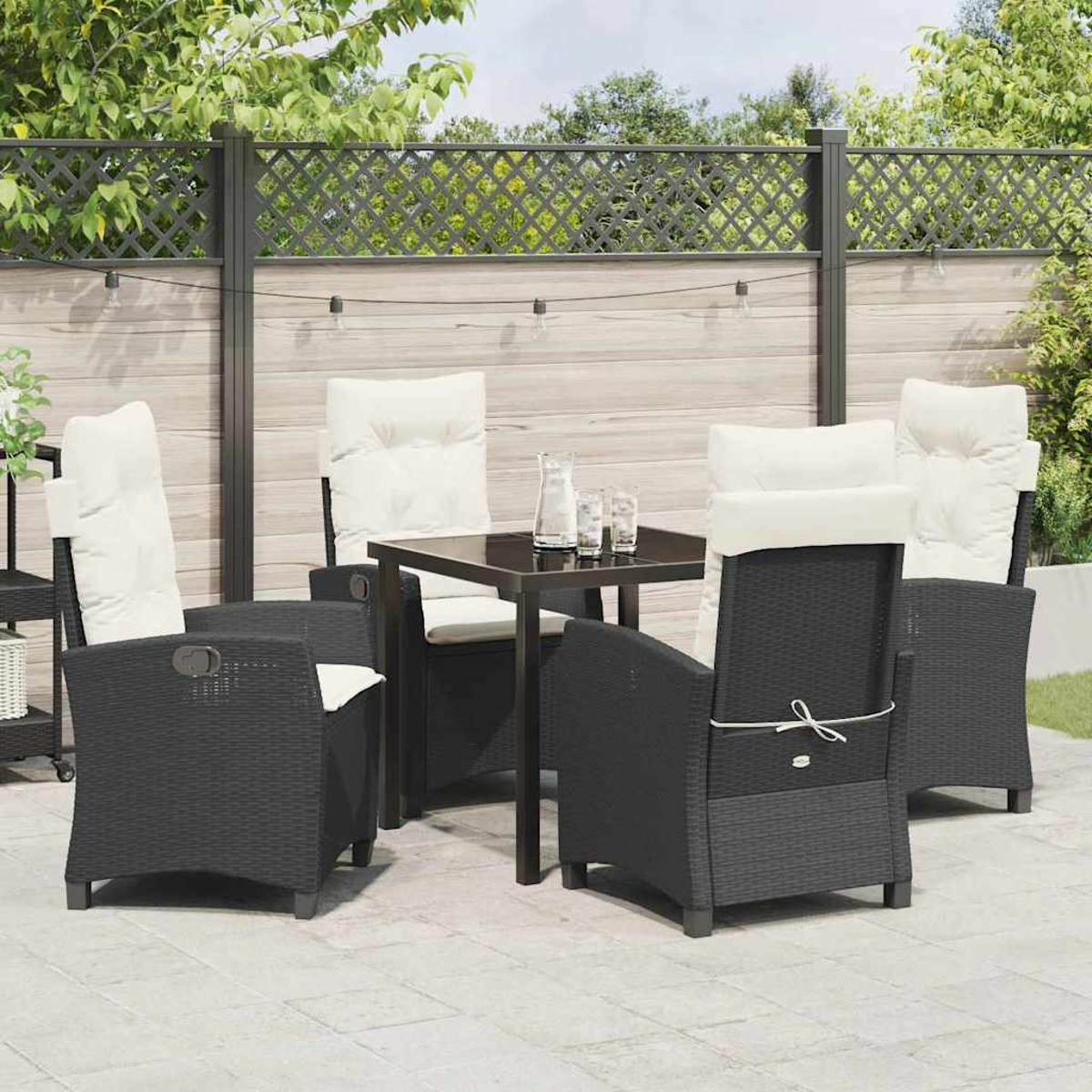 Terrassenset im Freien mit schwarzen Korbstühlen, weißen Kissen und einem schwarzen Tisch. Enthält einen dekorativen Zaun und Lichterketten.