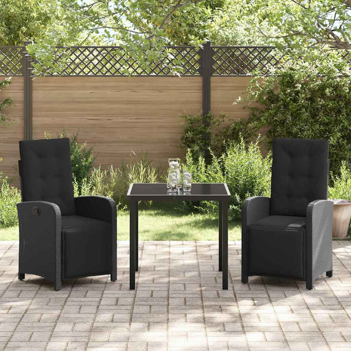 Zwei schwarze Liegestühle und ein Tisch auf einer gepflasterten Terrasse. Im Hintergrund ein Holzzaun und Grün.