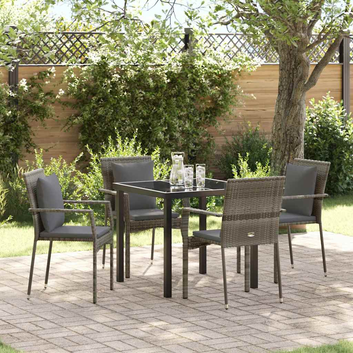 Terrassenset im Freien: quadratischer Tisch mit vier Stühlen. Ein Krug und zwei Gläser auf dem Tisch. Grüne Pflanzen und Bäume im Hintergrund.