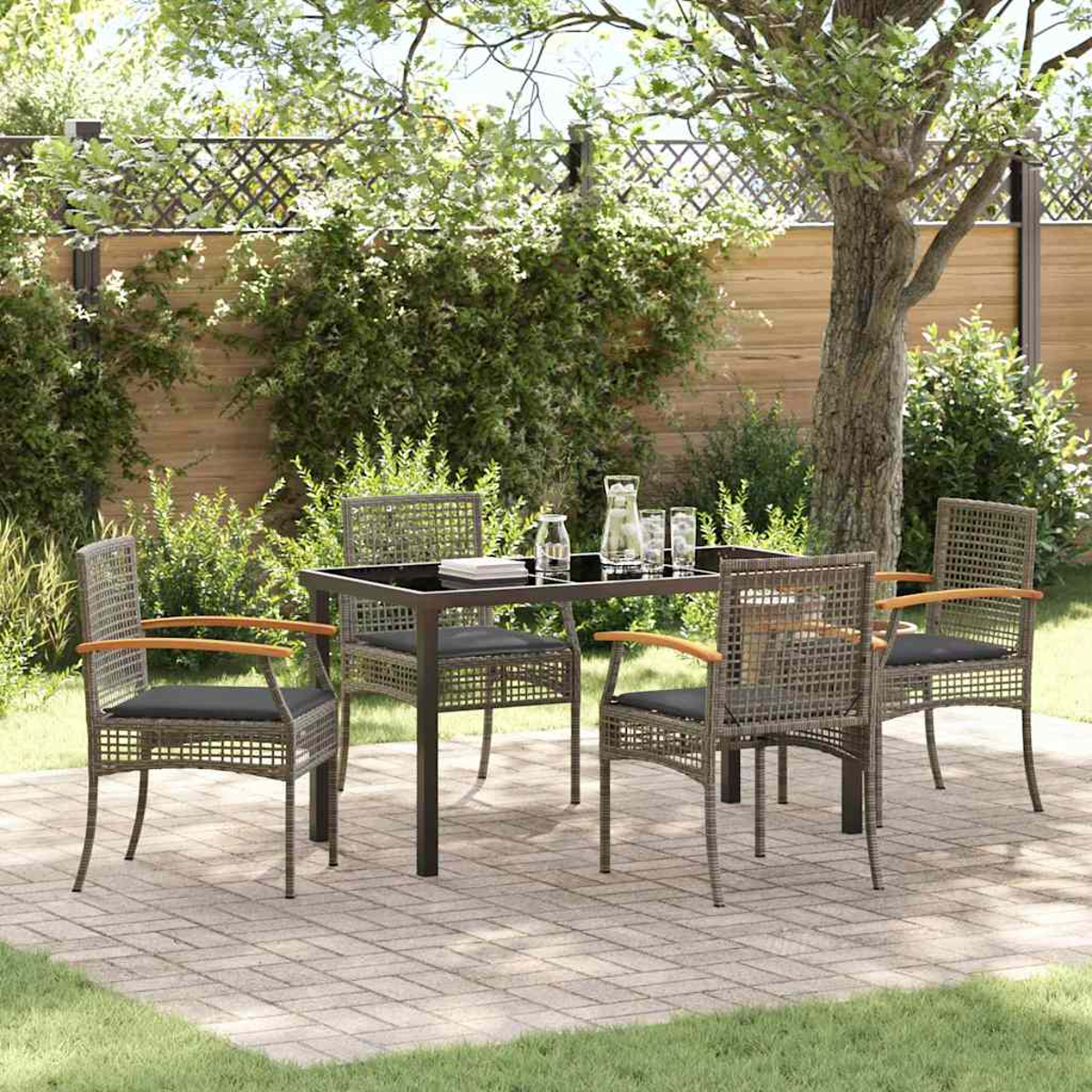 Set da pranzo all'aperto con tavolo e sedie su un patio in mattoni. Sfondo: recinzione in legno, alberi e vegetazione.