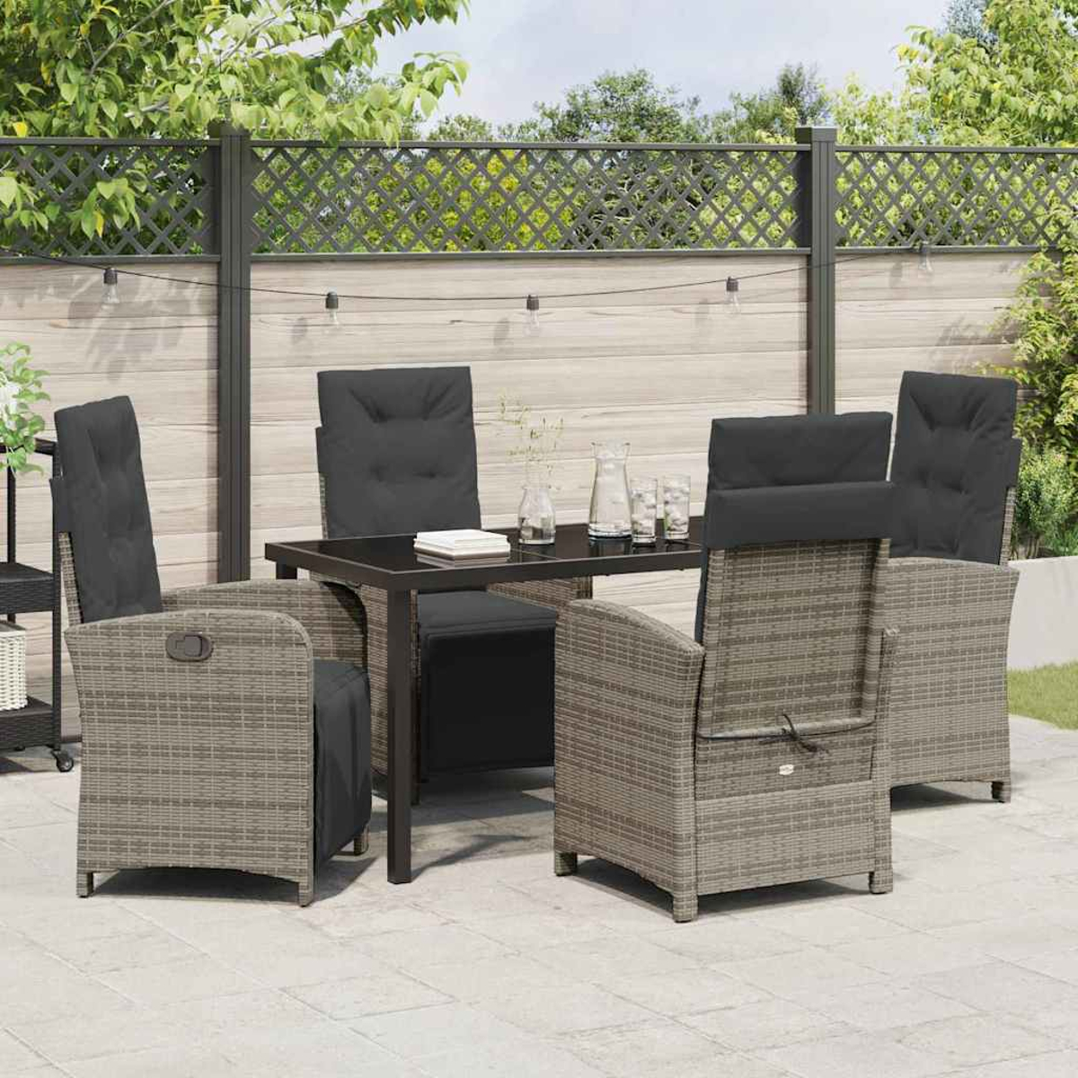 Essgruppe im Freien mit schwarzem Tisch und sechs grauen Korbstühlen mit schwarzen Kissen, auf einer Terrasse vor einem Zaun.