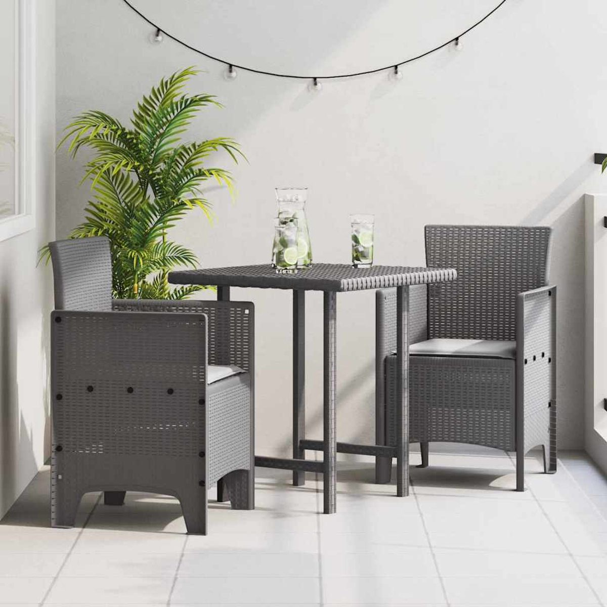 Terrassenset im Freien. Grauer Tisch und Stühle. Getränke mit Limetten auf dem Tisch. Palmenpflanze im Hintergrund. Lichterkette darüber.