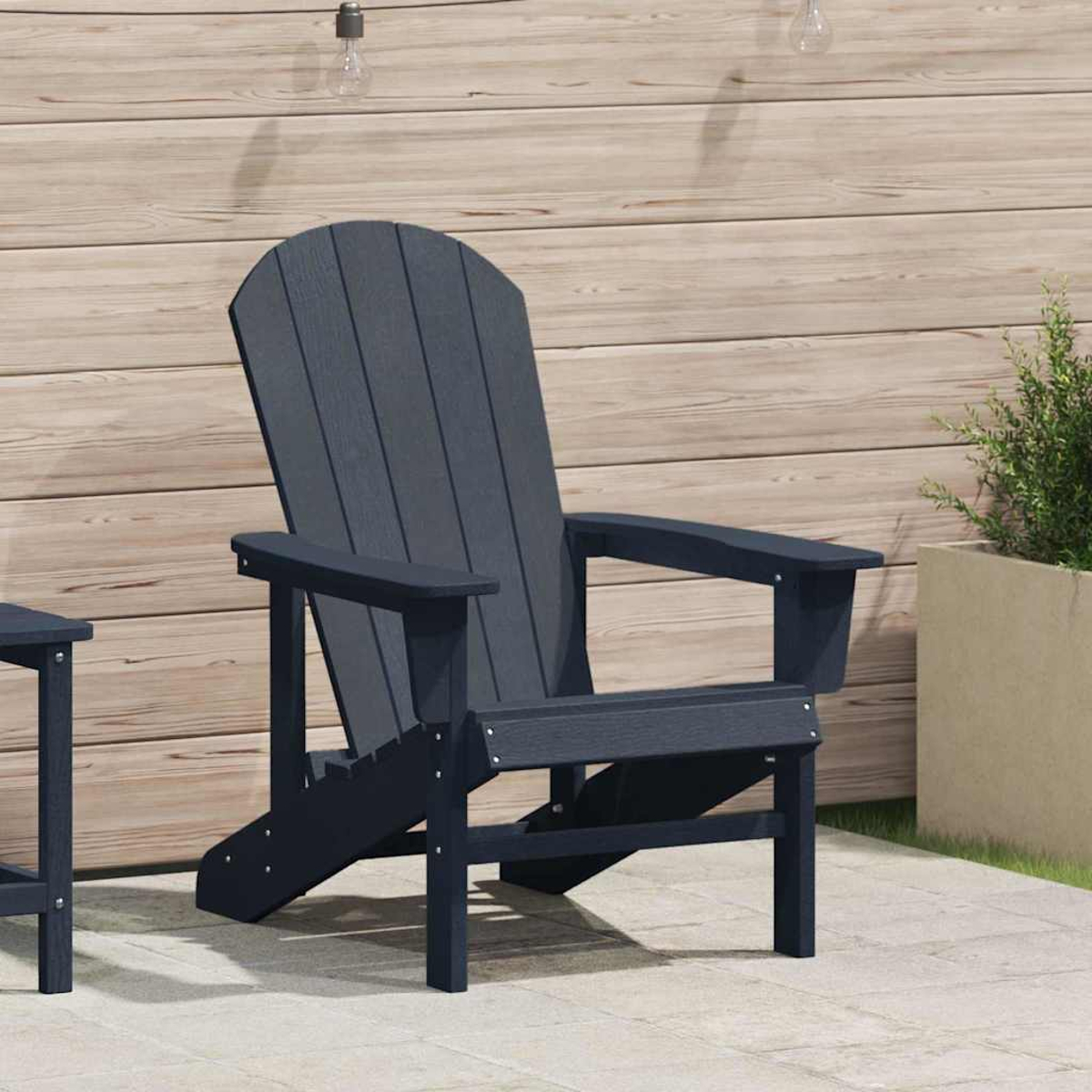 Ein dunkelblauer Adirondack-Stuhl steht auf einer Terrasse. Im Hintergrund befindet sich eine Holzwand, rechts ein Topf mit Pflanzen.