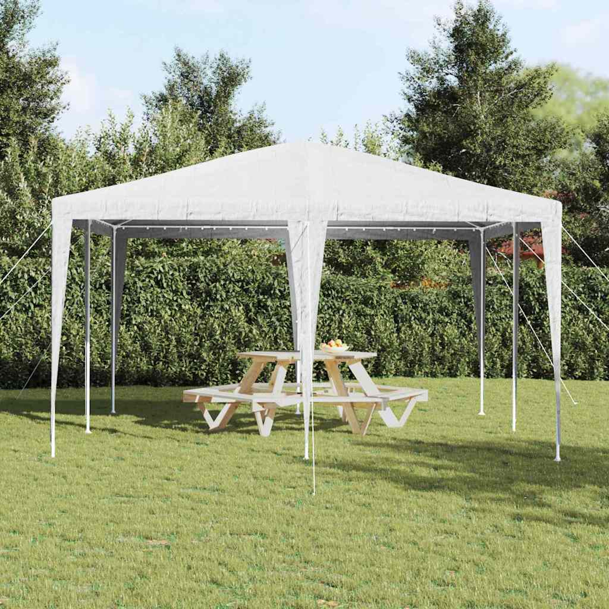 Un tendone bianco sopra un tavolo da picnic in legno su erba verde. Alberi e cespugli formano lo sfondo. Frutta sul tavolo.