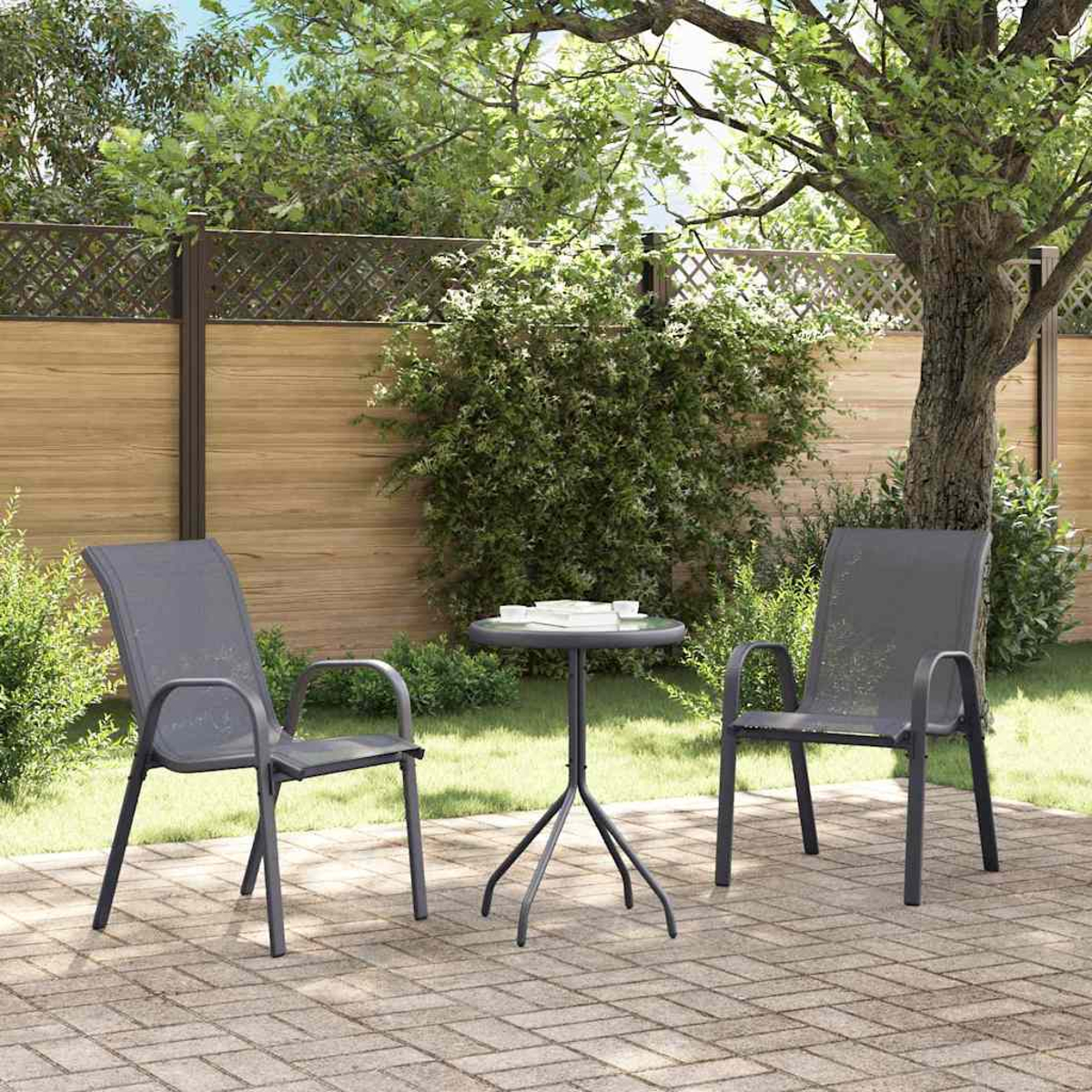 Due sedie grigie e un tavolino su un patio in mattoni in un giardino. Una staccionata in legno e alberi verdi sullo sfondo.