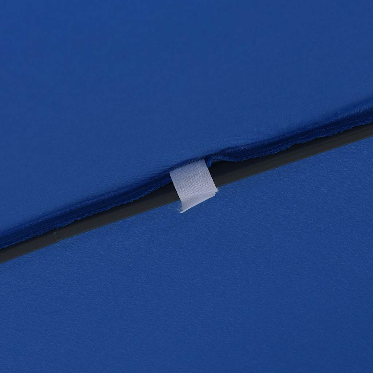 Primo piano di tessuto blu, una linea scura e una linguetta in velcro bianca. Il tessuto è strutturato. L'attenzione è sulla linguetta.