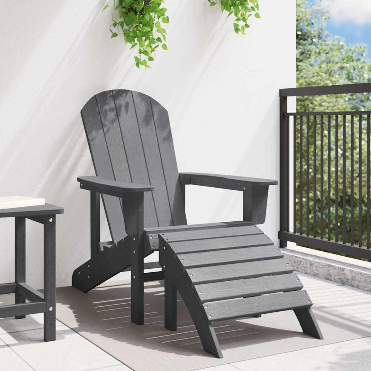 Una silla Adirondack gris con reposapiés en un patio. Una mesita a la izquierda. Plantas verdes cuelgan de arriba.