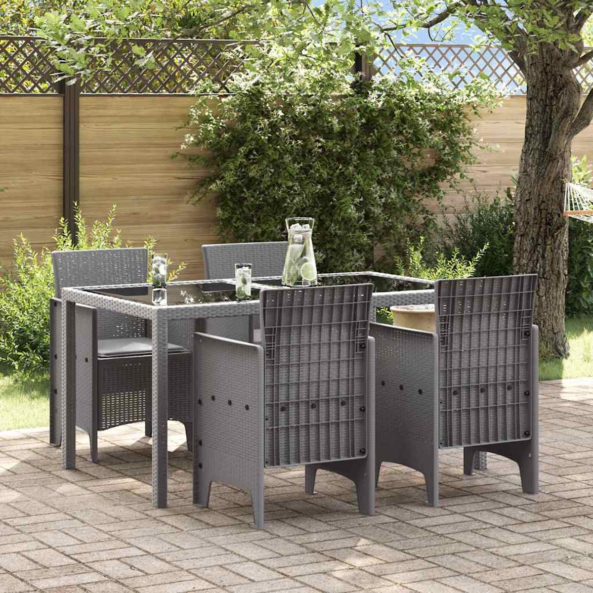 Set da pranzo all'aperto su un patio. Tavolo e sedie grigi, bevande e una recinzione sullo sfondo con fogliame verde.