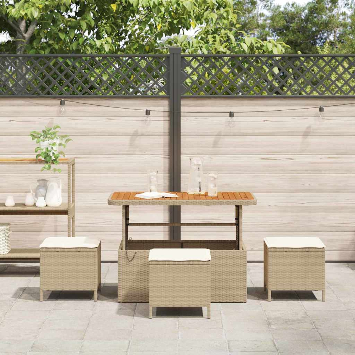 Terrassengarnitur mit Tisch und Hockern. Holztisch mit Gläsern. Korbstühle mit weißen Kissen. Holzzaun und Bäume im Hintergrund.