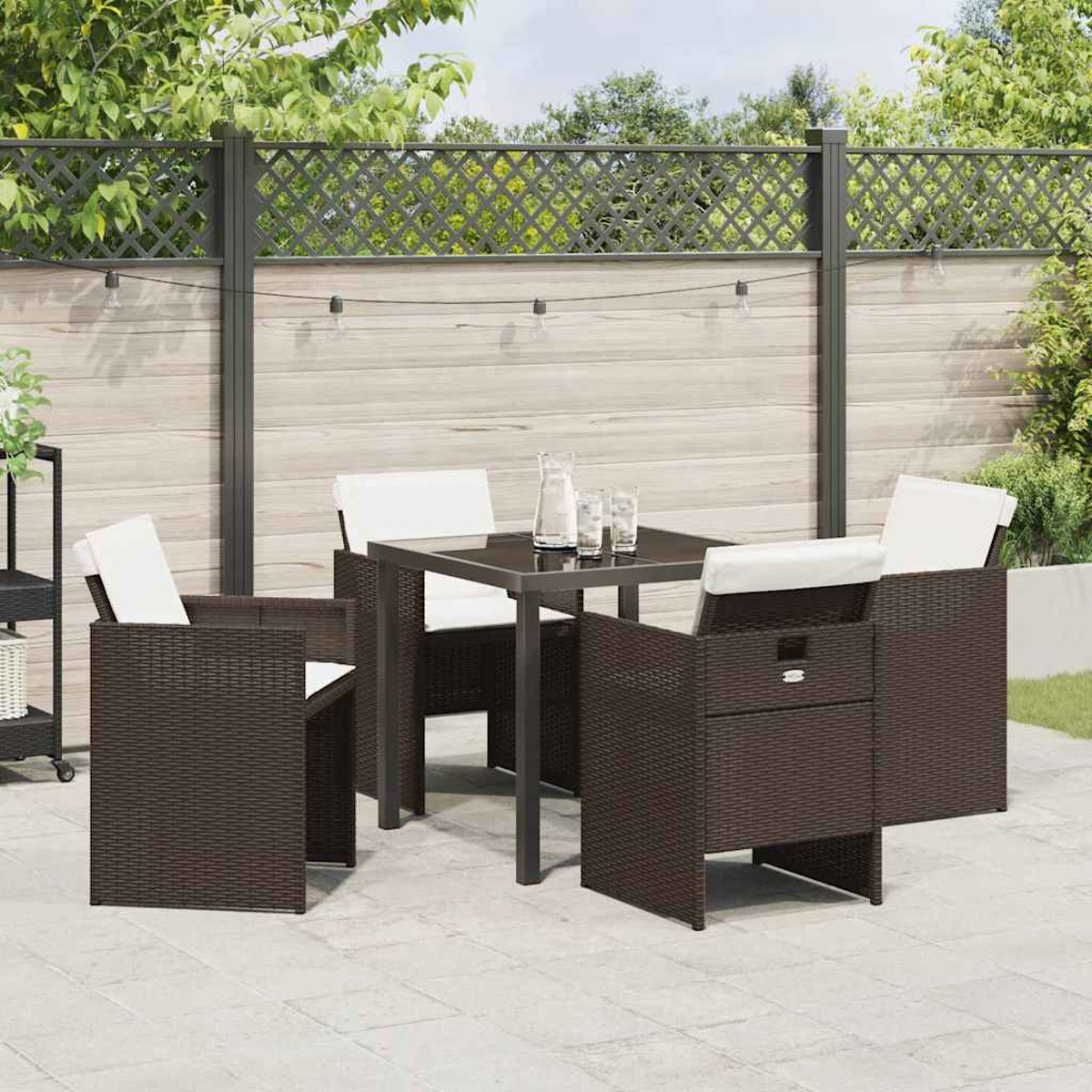 Set da patio all'aperto con tavolo e sedie marrone scuro con cuscini bianchi. Una recinzione e vegetazione sullo sfondo.