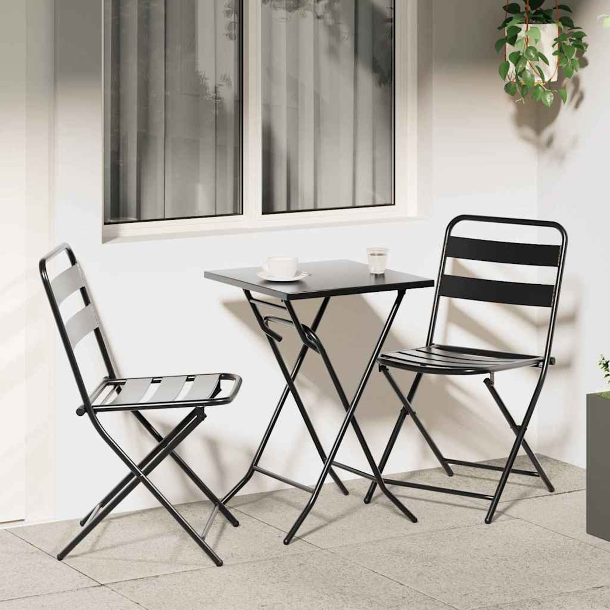 Szene im Freien mit schwarzem Metalltisch und Stühlen. Eine Tasse und ein Glas stehen auf dem Tisch. Fenster im Hintergrund, Pflanze darüber.