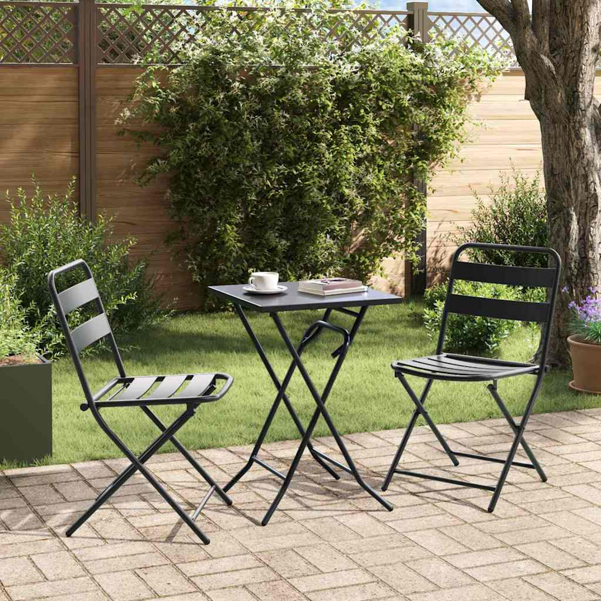Ein schwarzer Tisch und zwei Stühle auf einer Terrasse. Auf dem Tisch stehen eine Tasse und ein Buch. Im Hintergrund grünes Gras und ein Holzzaun.