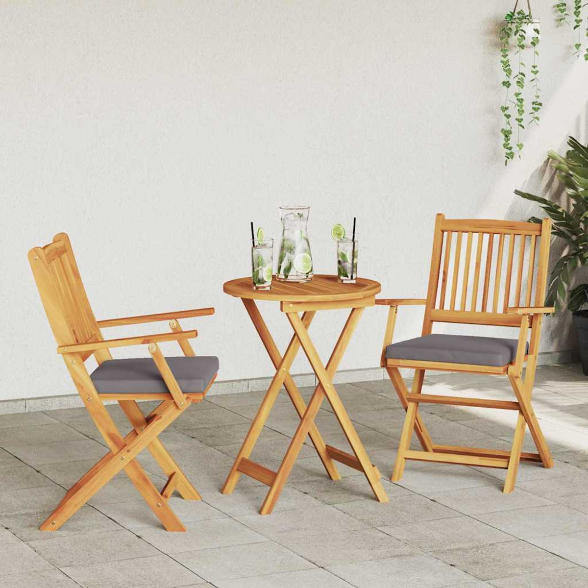 Ein Holz-Terrassenset mit rundem Tisch, zwei Stühlen mit grauen Kissen und Getränken. Im Hintergrund hängen grüne Pflanzen.
