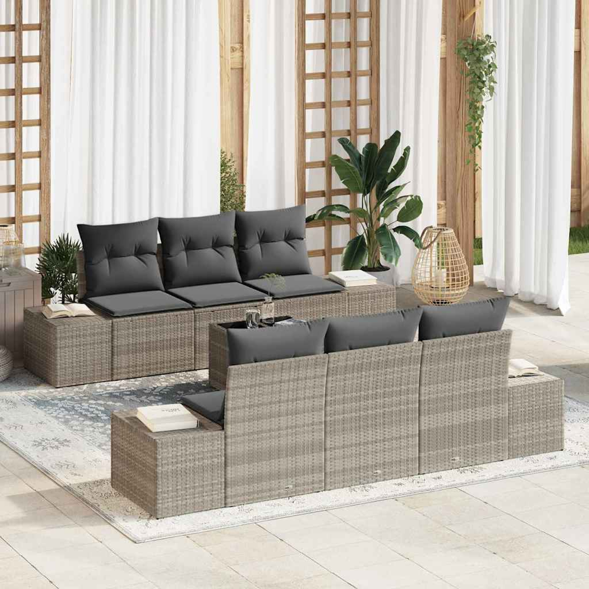 Outdoor-Korbmöbel-Set mit grauen Kissen. Enthält Sofas, Beistelltische und eine dekorative Laterne, vor weißen Vorhängen und Pflanzen.