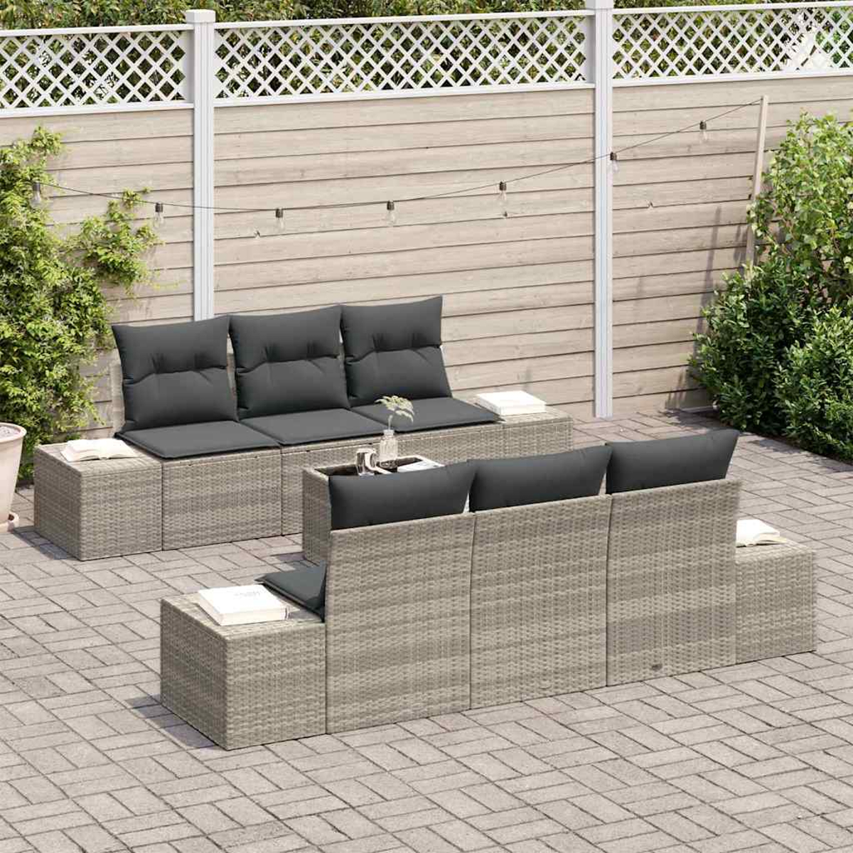 Gartenmöbel-Set: graue Korbsessel mit dunkelgrauen Kissen, auf einer Ziegelterrasse, mit weißem Zaun und Grün.