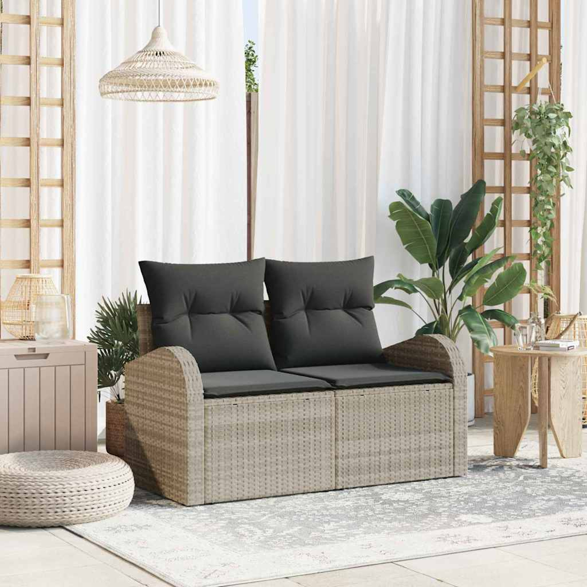 Rattansofa mit grauen Kissen, Pflanzen und einer Hängelampe. Weiße Vorhänge im Hintergrund. Holzgitter und ein kleiner Tisch.