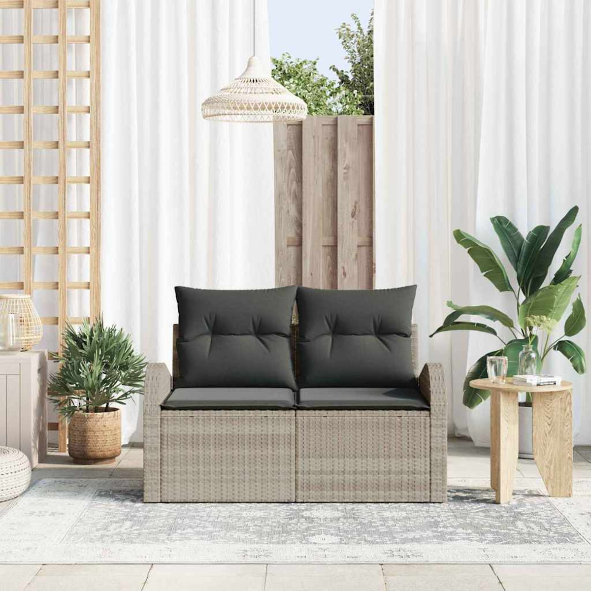 Szene im Freien mit einem grauen Korbliegesofa mit dunkelgrauen Kissen. Ein Holztisch, Pflanzen, Vorhänge und ein Teppich sind ebenfalls sichtbar.