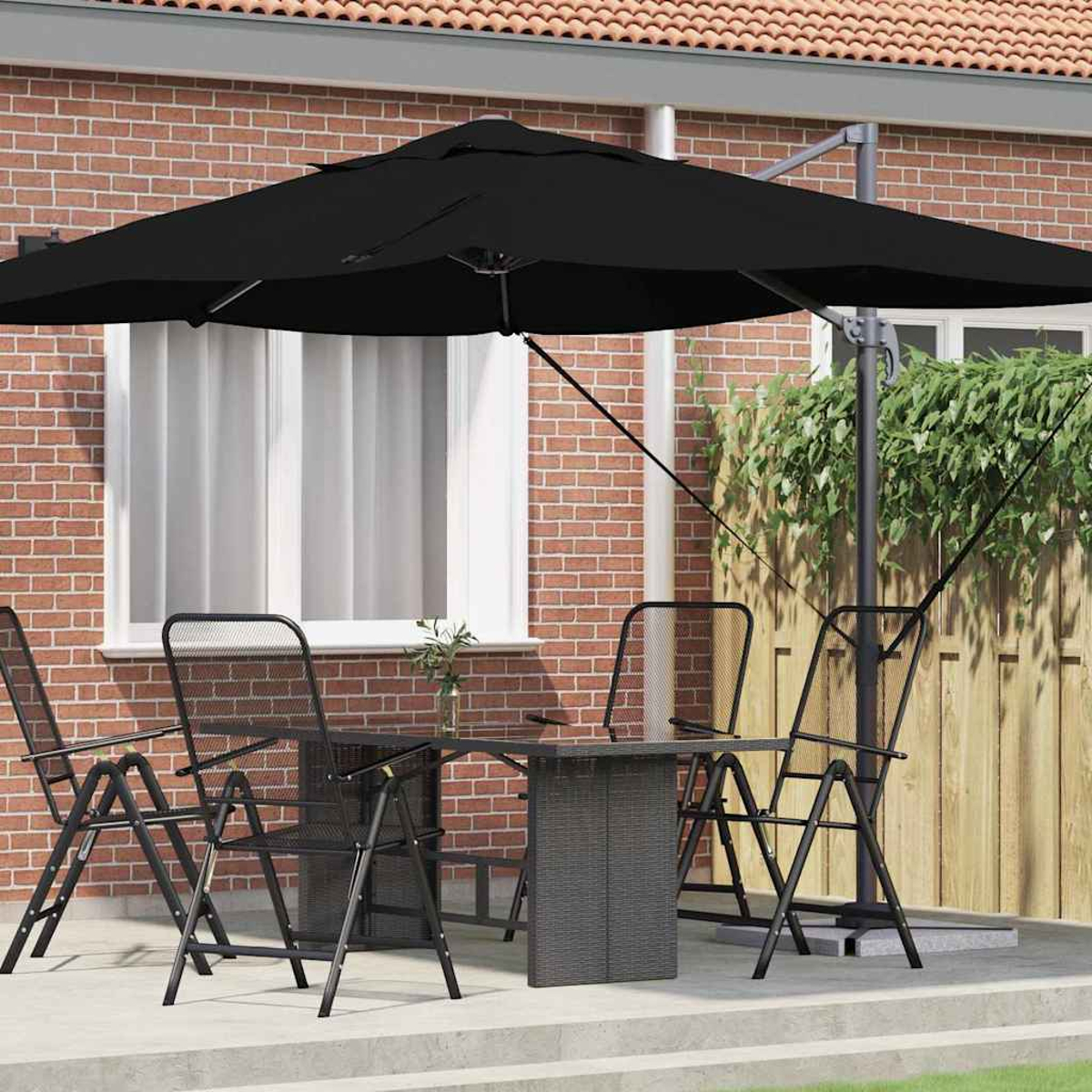 Un ombrellone nero ombreggia un set da patio con quattro sedie e un tavolo. Un muro di mattoni e una recinzione di legno formano lo sfondo.