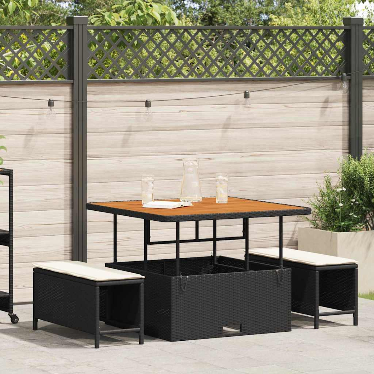 Terrassenmöbel-Set mit Holztisch, schwarzen Korbsesseln und Zierzaun. Kanne und Gläser stehen auf dem Tisch.