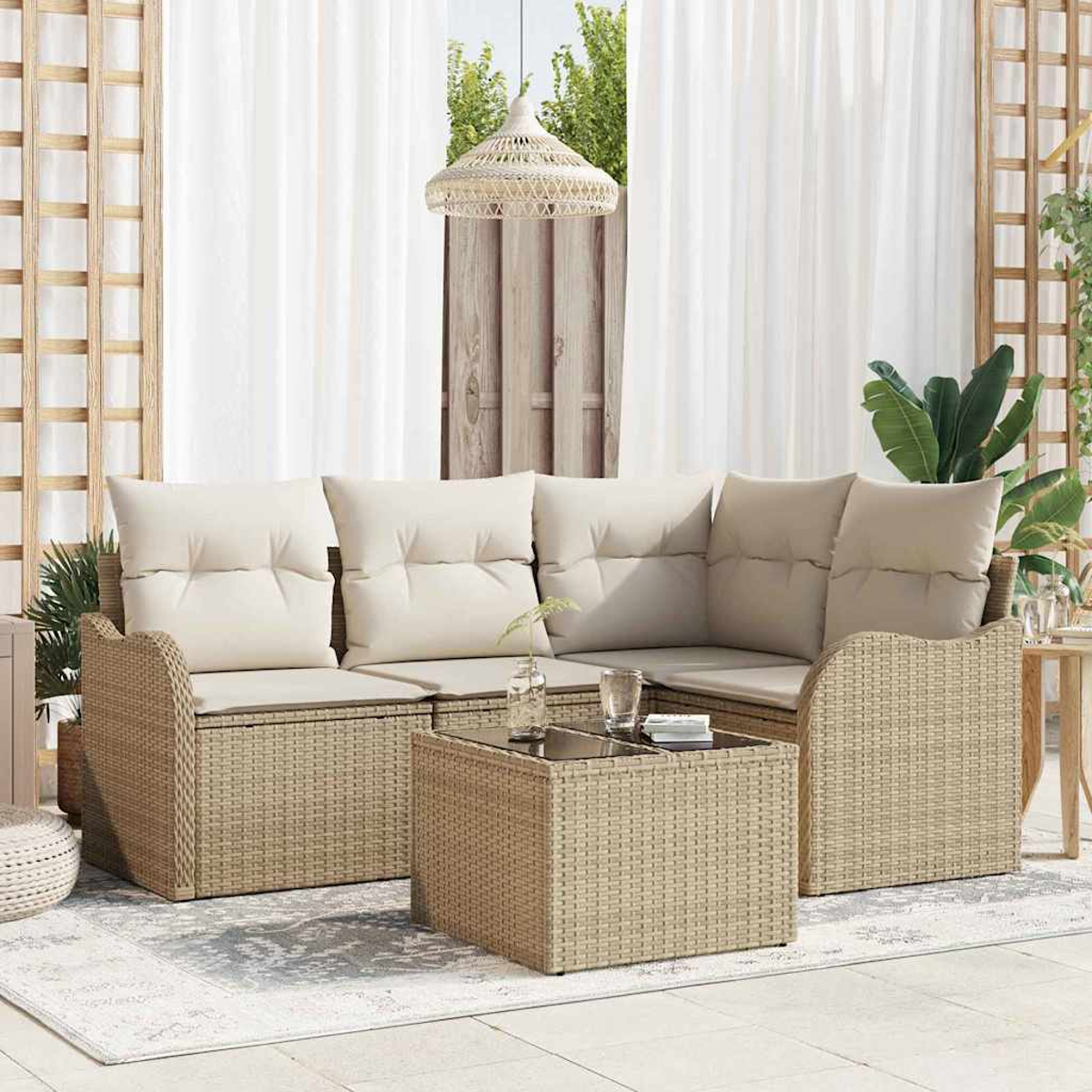 Outdoor-Korbmöbelset mit beigen Kissen und Couchtisch. Weiße Vorhänge und Pflanzen befinden sich im Hintergrund.