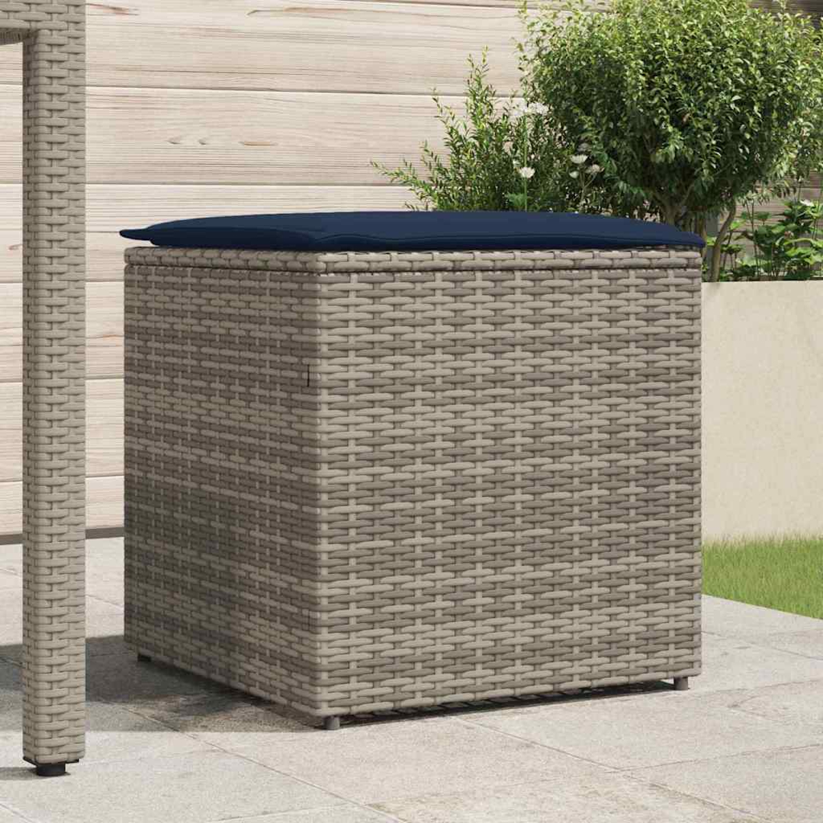 Eine Aufbewahrungsbox aus Korbgeflecht mit einem blauen Kissen. Sie steht auf einer Terrasse mit Holzwand und Grün im Hintergrund.