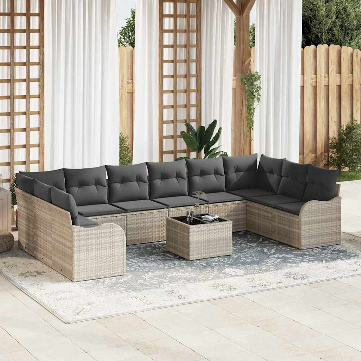 Outdoor-Ecksofa mit grauen Kissen auf einem gemusterten Teppich. Weiße Vorhänge und ein Holzzaun im Hintergrund.