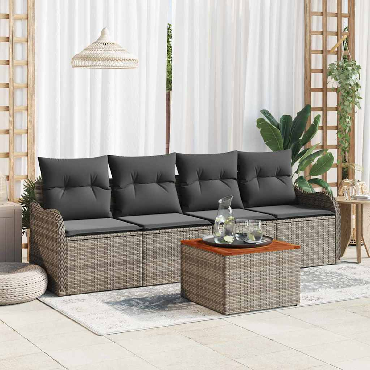 Rattansofa mit grauen Kissen, Couchtisch und weißen Vorhängen. Pflanzen und eine Hängeleuchte sind ebenfalls sichtbar. Outdoor-Patio-Setting.
