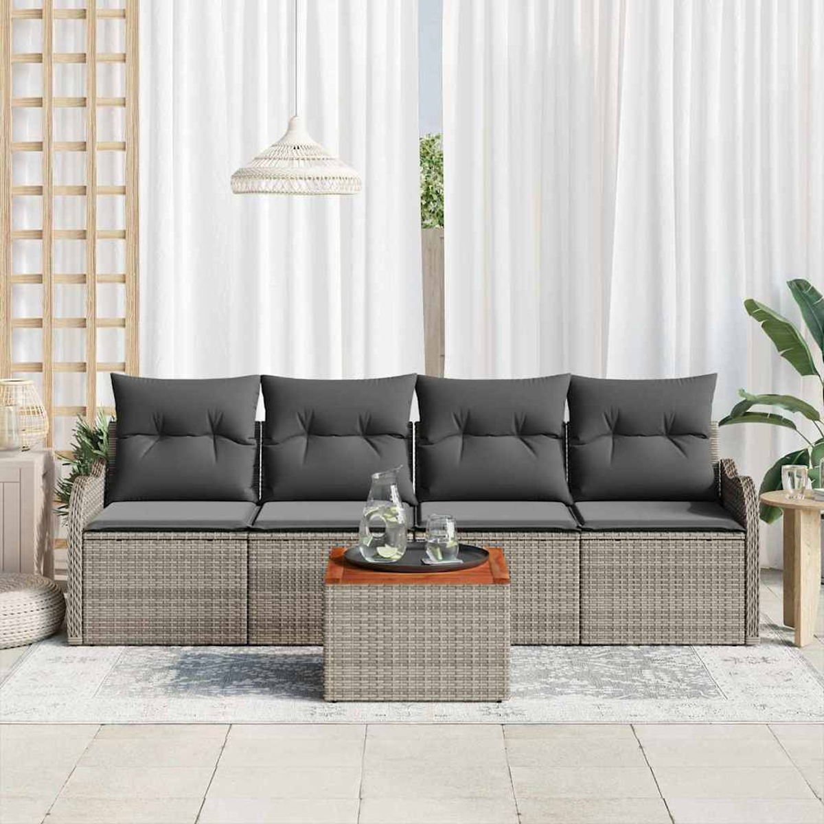 Rattan-Sofa im Freien mit grauen Kissen, Holztisch mit Getränken, weißen Vorhängen und einer Hängelampe. Rechts ist eine Pflanze.