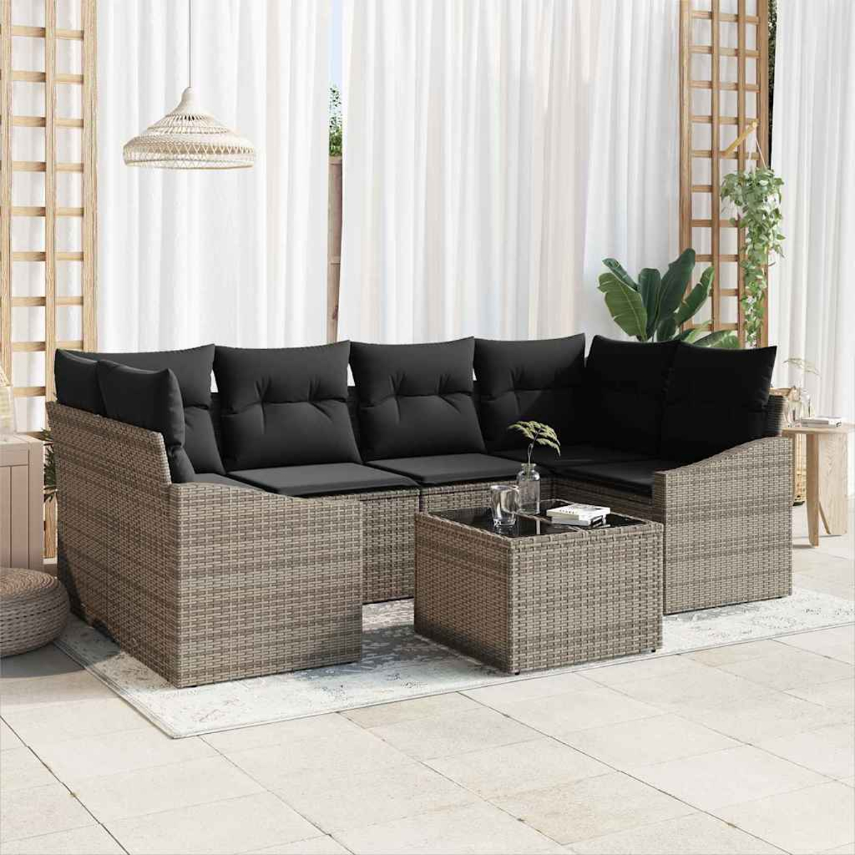 Outdoor-Geflechtsitzgruppe mit schwarzen Kissen, einem quadratischen Tisch und durchsichtigen weißen Vorhängen im Hintergrund.