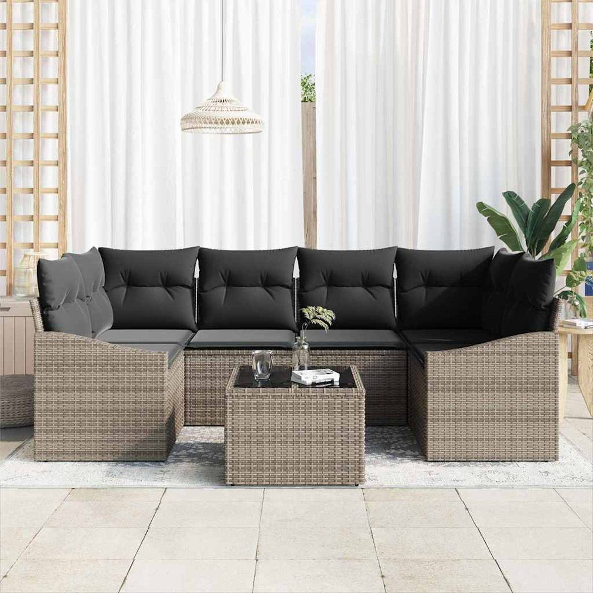 Outdoor-Korbsessel mit schwarzen Kissen und einem Tisch mit Glasplatte. Weiße Vorhänge und eine Pendelleuchte im Hintergrund.