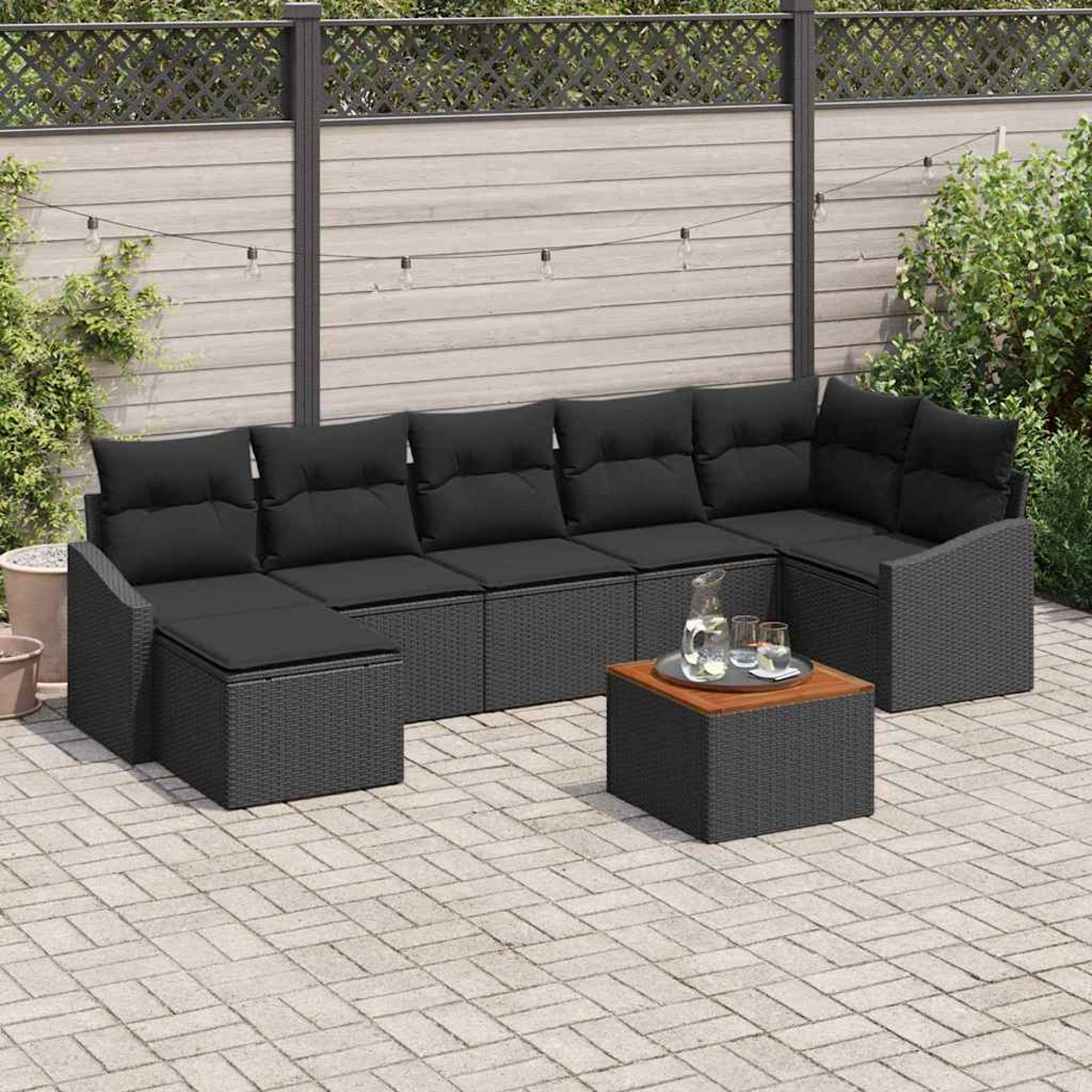 Outdoor-Ecksofa-Set mit schwarzen Kissen, einem quadratischen Tisch und einem Krug mit Gläsern auf einer Terrasse.