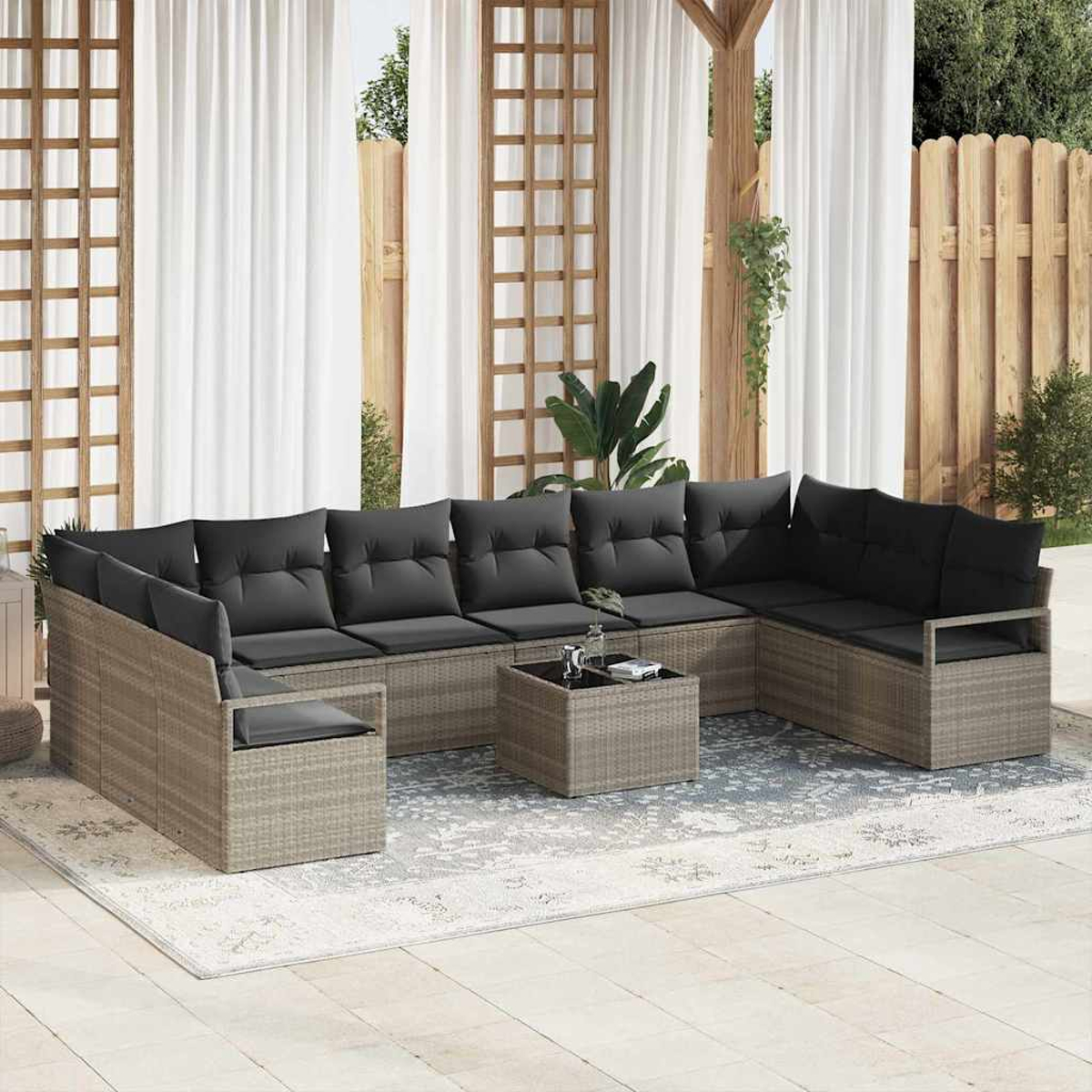Outdoor-Sitzgruppe mit grauen Kissen. Ein Couchtisch steht in der Mitte. Weiße Vorhänge und ein Holzzaun sind im Hintergrund.